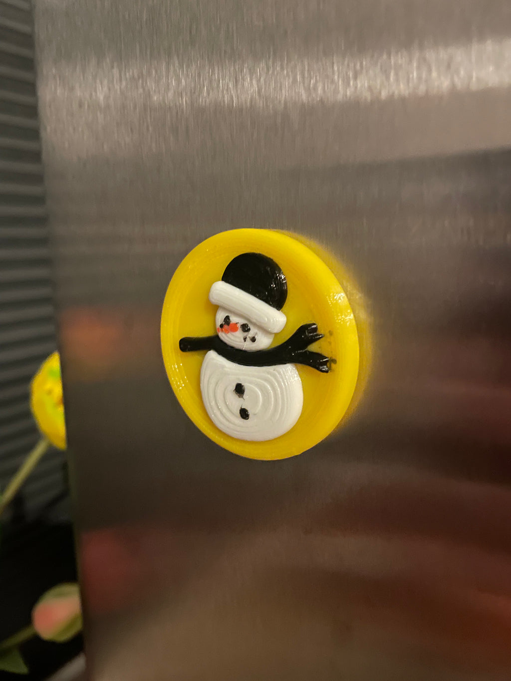 3D-geprinte sneeuwpop koelkastmagneet met een vrolijke gele achtergrond.